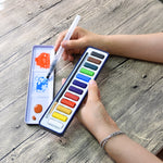A person using the aqua brush to test paint colours on the lid of the artist series watercolour paint set that has 12 colours - Stationery Island