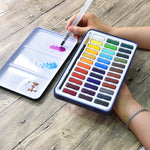 A person using the aqua brush to test paint colours on the lid of the artist series watercolour paint set that has 36 colours - Stationery Island